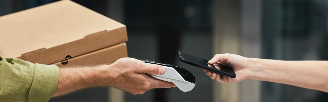 Side view closeup of unrecognizable client paying for delivery service via smartphone NFC, copy space